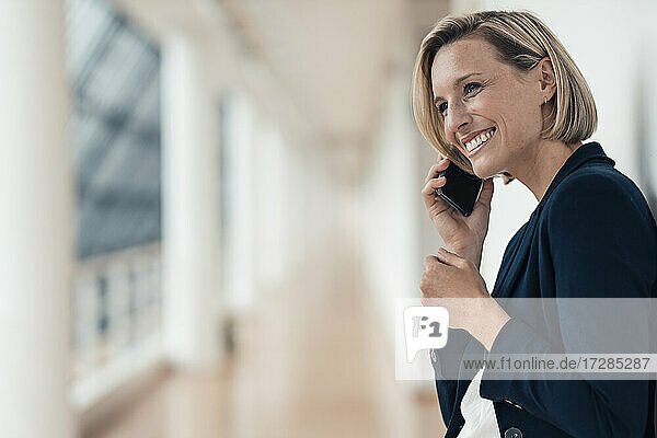 Unternehmerin lächelt  während sie im Büro mit dem Handy telefoniert