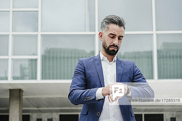Geschäftsmann prüft vor einem Gebäude die Zeit auf seiner Armbanduhr