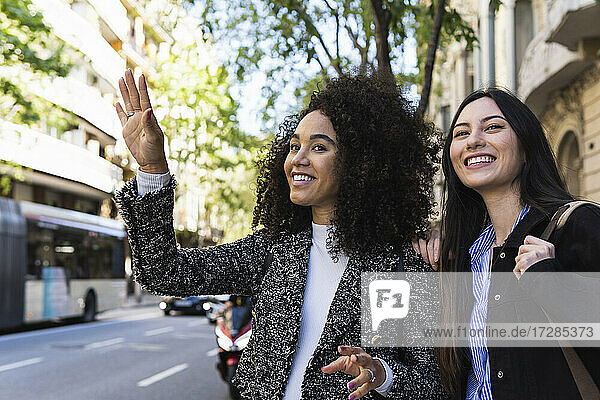 Lächelnde Freundinnen hailing Fahrt auf der Straße