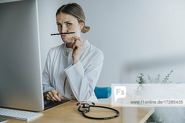 Weiblicher Arzt spielt mit Stift  während er am Schreibtisch sitzt