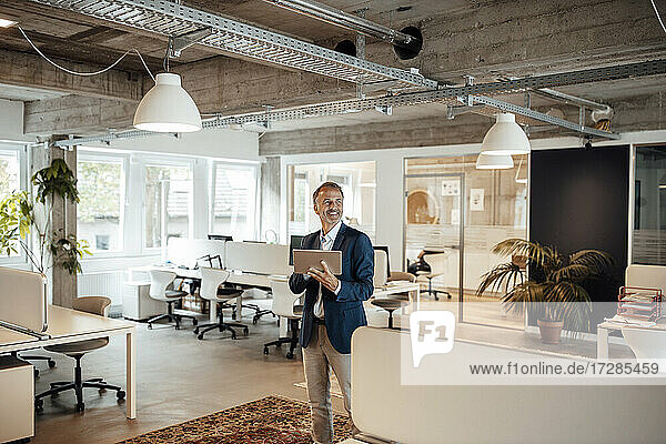 Lächelnder Geschäftsmann  der ein digitales Tablet hält  während er im Büro steht