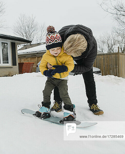 Liebevoller Vater umarmt seinen Sohn  der im Winter Snowboarden lernt