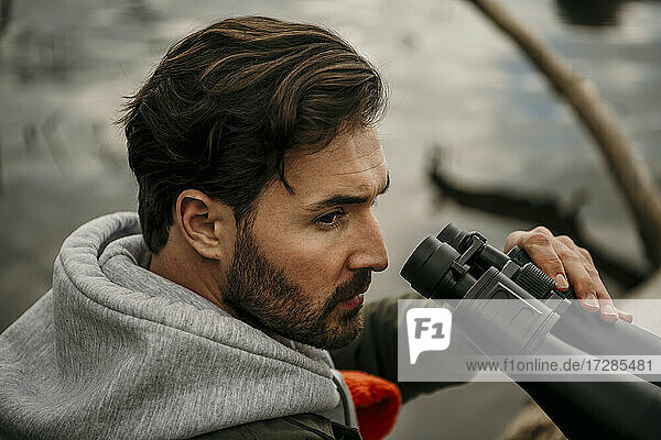 Handsome man with beard holding binoculars while looking away