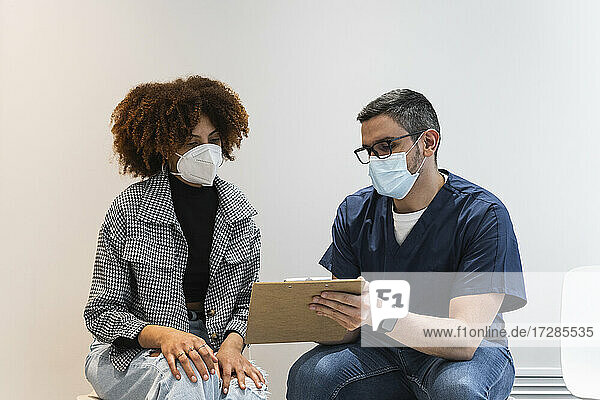 Ein männlicher Zahnarzt erklärt einer Patientin während einer Pandemie in einer Klinik einen medizinischen Bericht