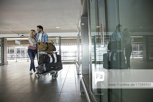 Glückliches junges Paar mit Gepäckwagen im Flughafenterminal