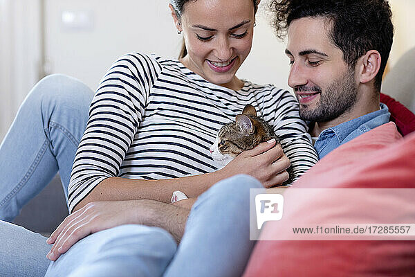 Lächelndes Paar mit getigerter Katze im heimischen Wohnzimmer