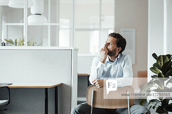 Thoughtful male entrepreneur looking away while sitting on chair at office