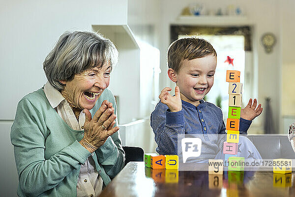 Fröhliche Großmutter und Enkel jubeln beim Spielen mit Bauklötzen zu Hause