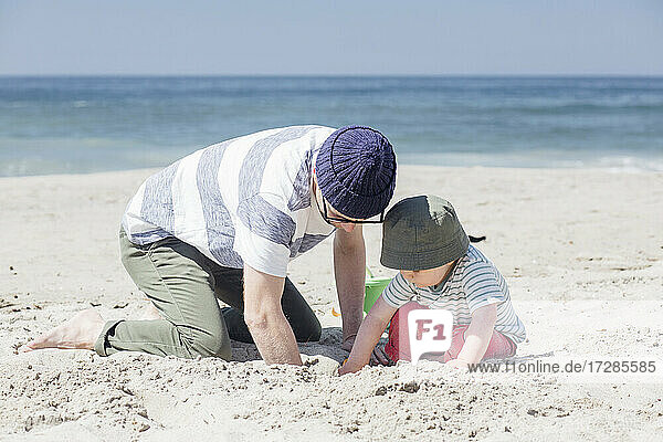Vater und Sohn graben gemeinsam im Sand  während sie an einem sonnigen Tag am Strand spielen