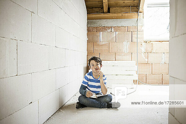 Thoughtful boy with book sitting on loft floor during renovation