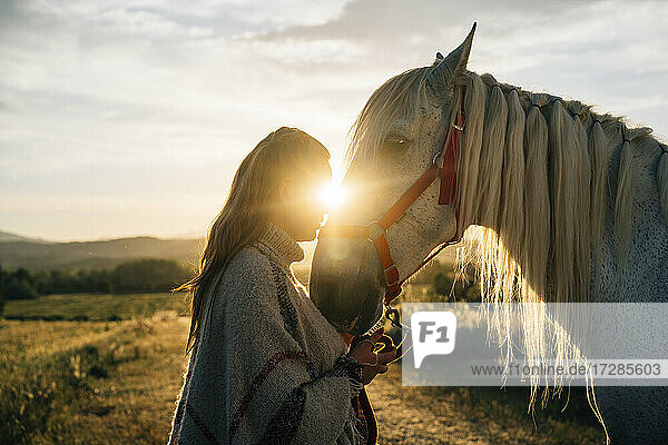 Frau umarmt Pferd auf einem Feld bei Sonnenuntergang