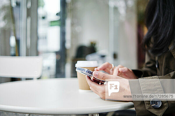 Frau benutzt Smartphone in einem Straßencafé