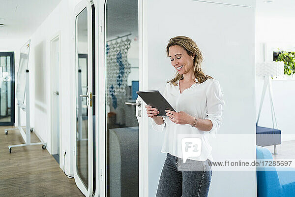 Lächelnde weibliche Fachkraft  die eine digitale Tafel in einer schalldichten Kabine im Büro betrachtet