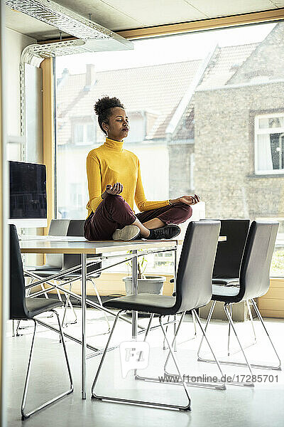 Unternehmerin im Schneidersitz beim Meditieren auf dem Schreibtisch im Büro