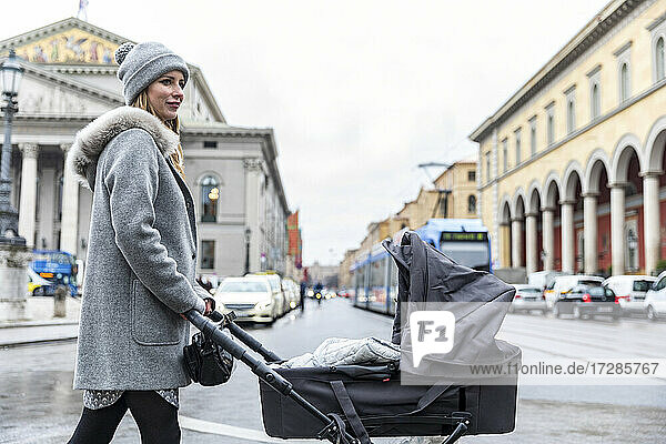 Frau in warmer Kleidung mit Kinderwagen auf der Straße in der Stadt
