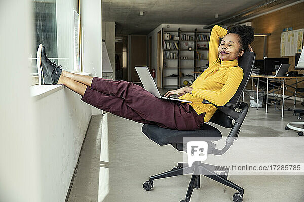 Businesswoman with laptop relaxing on chair at office apartment