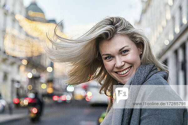 Lächelnde schöne blonde Frau  die sich die Haare wirft  während sie in der Stadt steht