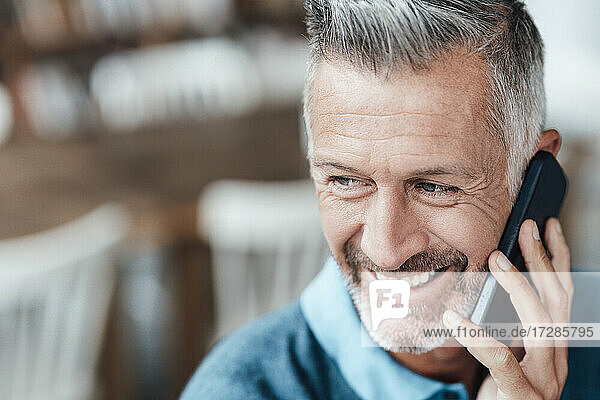 Älterer Geschäftsmann lächelt  während er in einem Café mit seinem Smartphone telefoniert