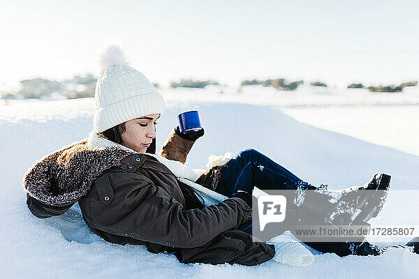 Frau hält Kaffeetasse und entspannt sich im Schnee im Urlaub