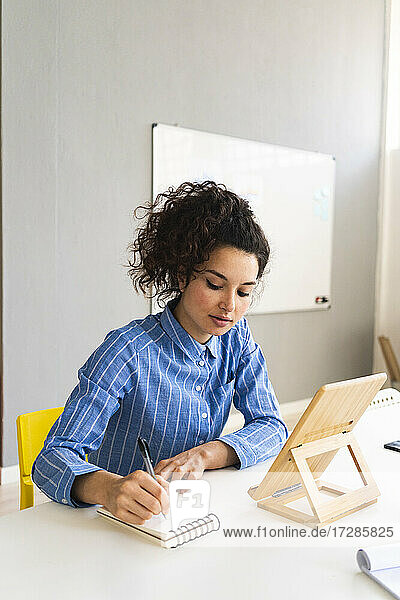 Geschäftsfrau mit digitalem Tablet  die in einen Notizblock schreibt  während sie im Kreativbüro arbeitet