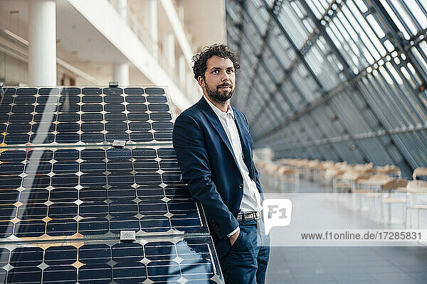 Geschäftsmann mit Händen in den Taschen  der sich auf ein Solarpanel stützt