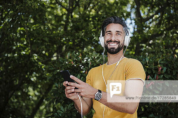 Smiling man with headphones and mobile phone standing at park