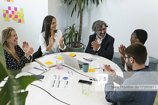 Lächelnde männliche und weibliche Fachkräfte klatschen während einer Besprechung im Büro