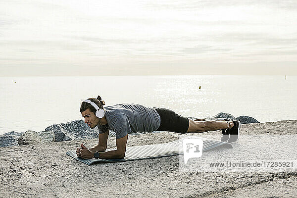 Male athlete with headphones exercising plank position on exercise mat
