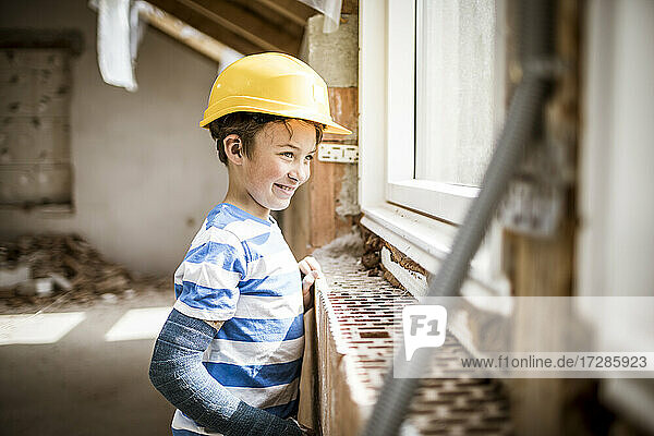 Junge mit Schutzhelm schaut durch ein Fenster auf einer Baustelle