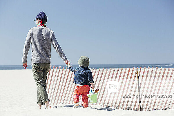 Vater und Sohn halten sich an den Händen  während sie an einem sonnigen Tag am Strand spazieren gehen