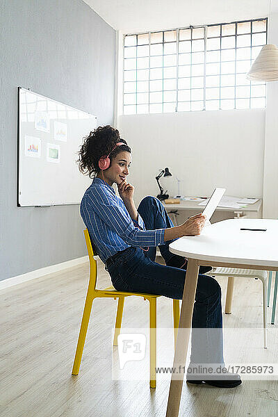 Geschäftsfrau mit Kopfhörern  die ein digitales Tablet im Kreativbüro benutzt