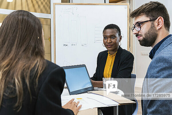 Männliche und weibliche Fachleute betrachten eine Geschäftsfrau  die während einer Besprechung im Büro diskutiert
