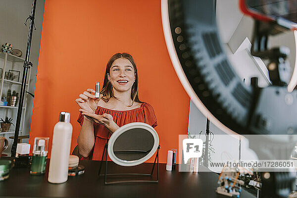 Lächelnde Influencerin präsentiert Lippenstift während eines Make-up-Tutorials bei Dreharbeiten zu Hause