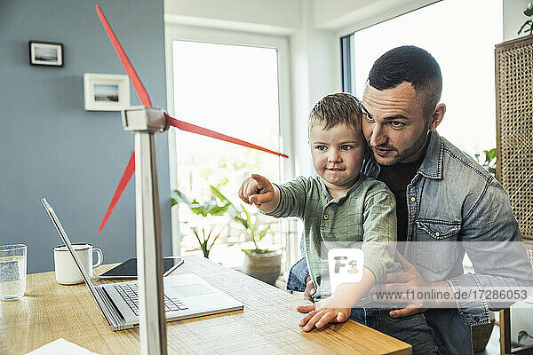 Boy pointing at wind turbine while sitting with father