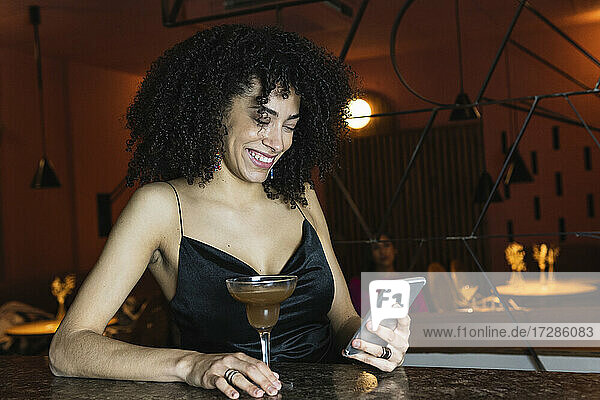 Lächelnde Frau  die ein Mobiltelefon bei einem Getränk auf dem Tisch benutzt