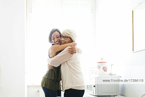 Happy grandmother hugging granddaughter in kitchen at home