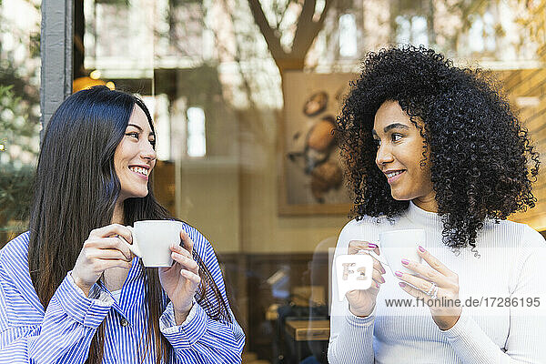 Smiling young woman looking at female friend while having coffee outside bar