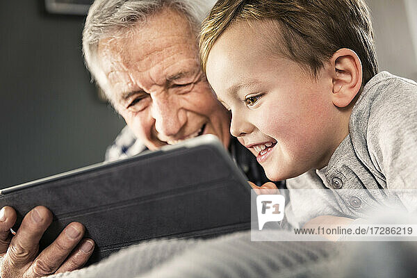 Lächelnder Junge benutzt digitales Tablet mit älterem Mann zu Hause