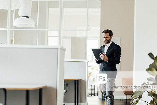 Männlicher Unternehmer  der im Stehen im Büro ein digitales Tablet benutzt