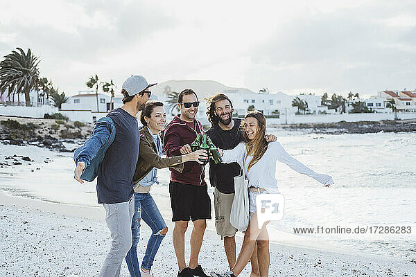 Glückliche Freunde stoßen mit Bierflaschen an  während sie am Strand stehen