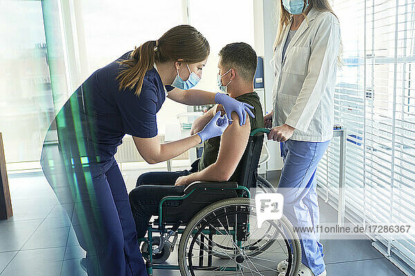 Eine Mitarbeiterin verabreicht einem männlichen Patienten  der im Rollstuhl sitzt  eine COVID-19-Impfdosis.