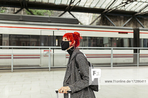 Rothaarige Frau mit Gesichtsschutzmaske am Bahnhof
