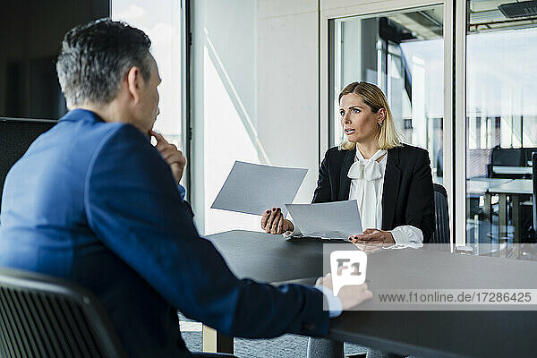 Businesswoman holding documents while discussing with colleague during meeting in board room