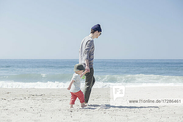 Vater und Sohn halten sich an den Händen und gehen am Strand spazieren