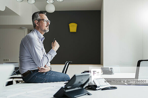 Male entrepreneur contemplating while sitting on desk