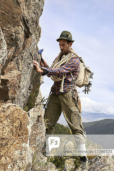 Männlicher Tourist mit Rucksack und Hammer an einem Felsen auf einem Berg stehend