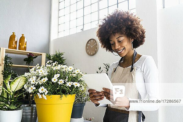 Eine Ladenbesitzerin benutzt ein digitales Tablet  während sie in einem Pflanzengeschäft steht.