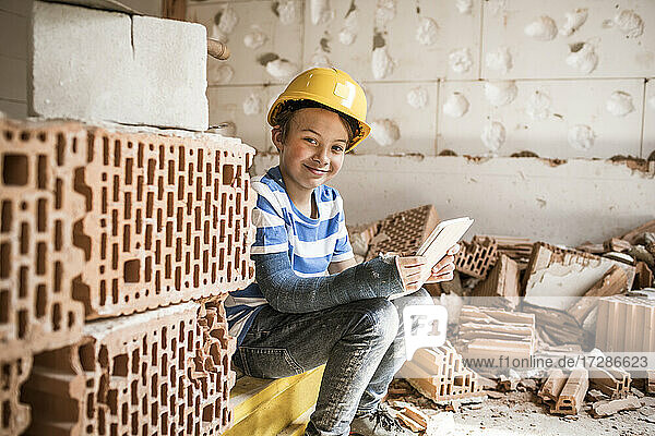 Lächelnder Junge mit Buch auf dem Dachboden während der Renovierung