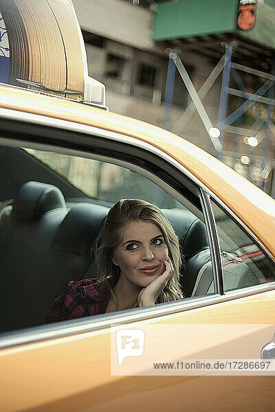 Lächelnde Frau mit Hand am Kinn  die durch das Fenster schaut  während sie im Taxi sitzt