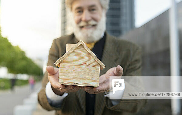 Lächelnder reifer Verkäufer zeigt Holzmodellhaus